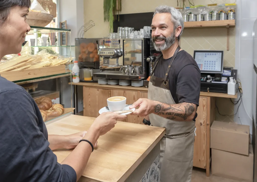 Barista sonriente entregando un café a una clienta en la barra