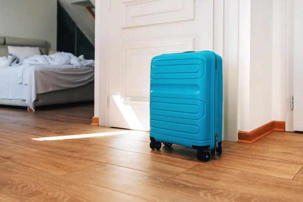 Maleta azul en el suelo de madera de un apartamento junto a la puerta abierta