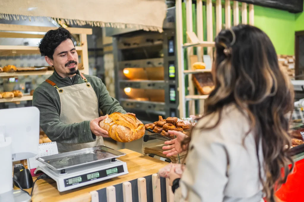 Panadero mostrando una hogaza a una clienta en el mostrador de una panadería