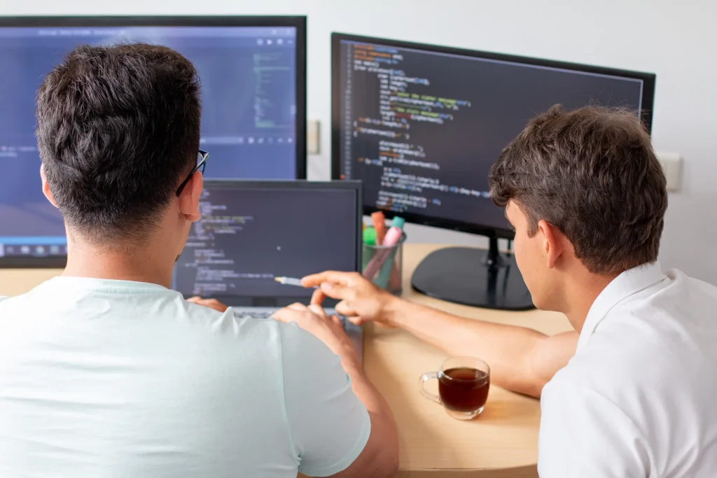 Dos programadores revisando código en varias pantallas