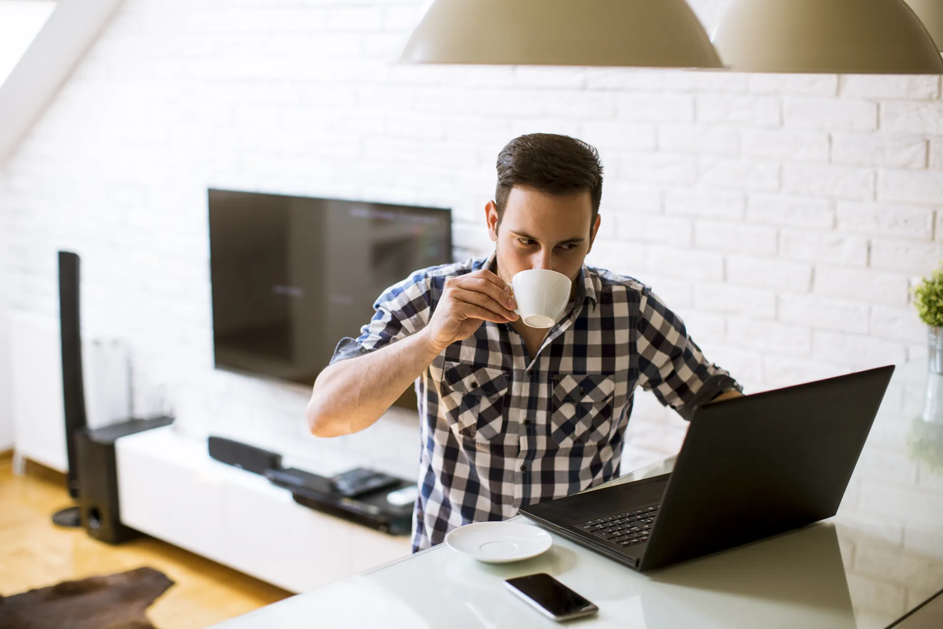 Hombre tomando un café mientras trabaja con su portátil en casa