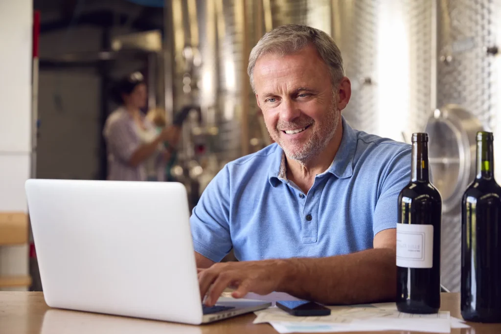 Responsable de una bodega trabajando con el portátil junto a botellas de vino