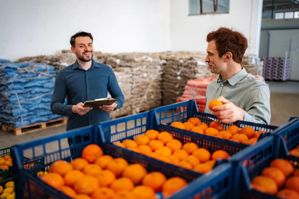 Dos trabajadores revisando cajas de naranjas en un almacén