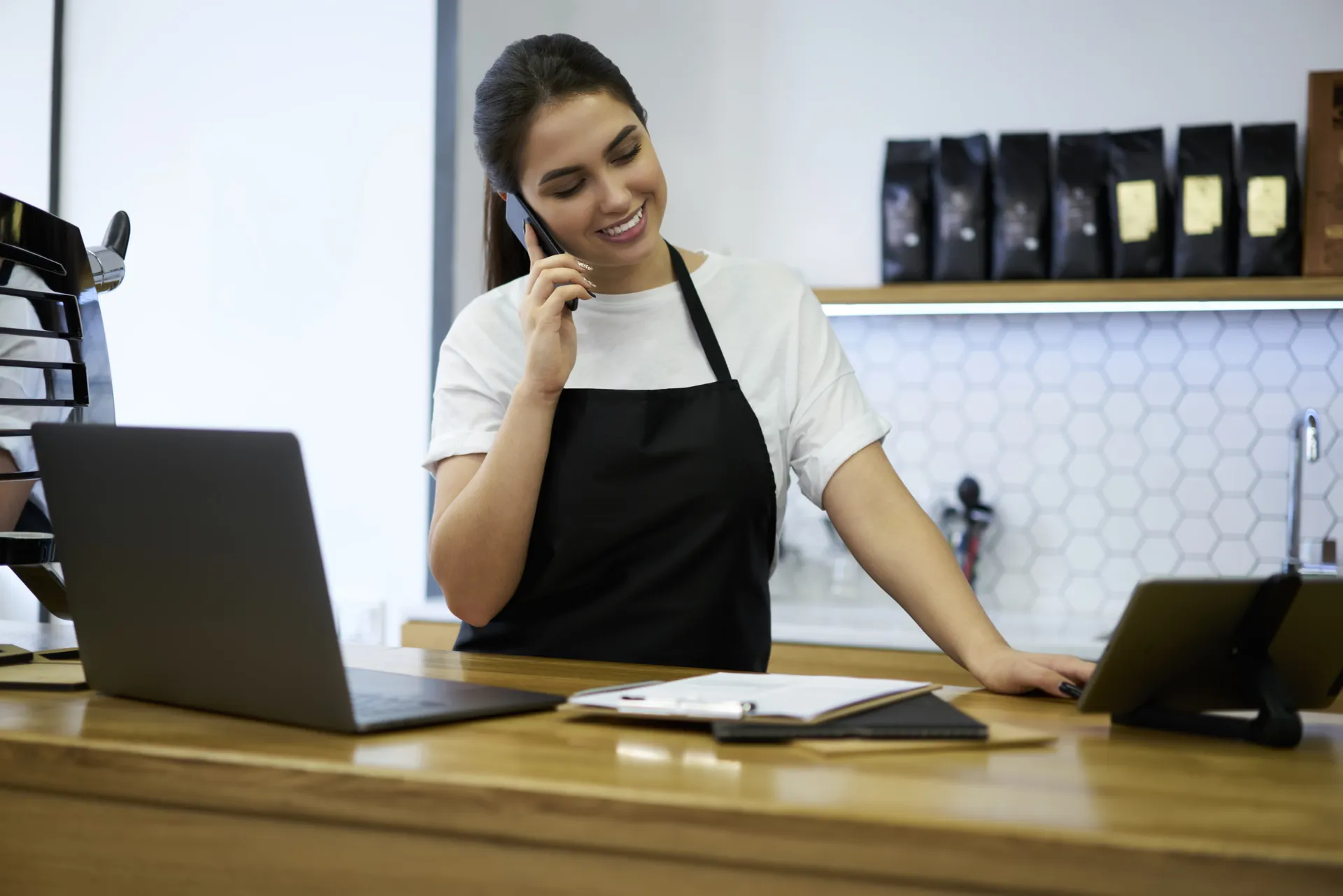 Responsable de una cafetería hablando por teléfono junto a su portátil en la barra