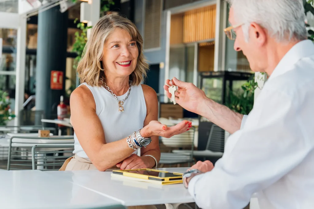 Mujer sonriente recibiendo unas llaves de un hombre mayor en una cafetería