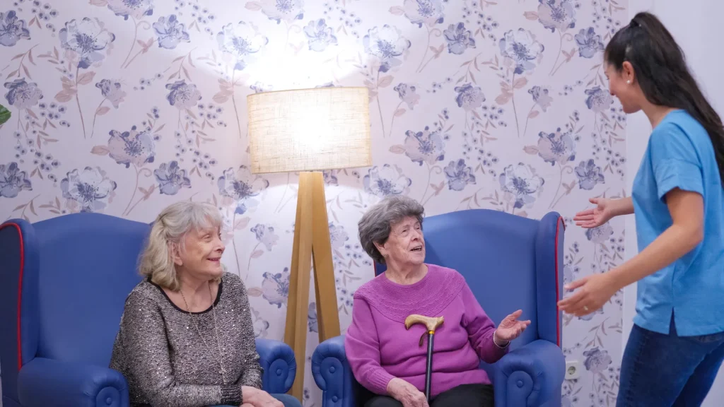 Cuidadora conversando con dos señoras mayores sentadas en sillones