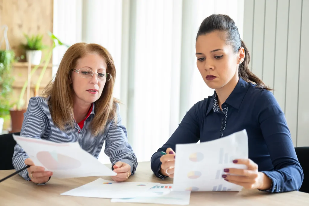 Dos compañeras revisando informes en papel en una mesa de trabajo
