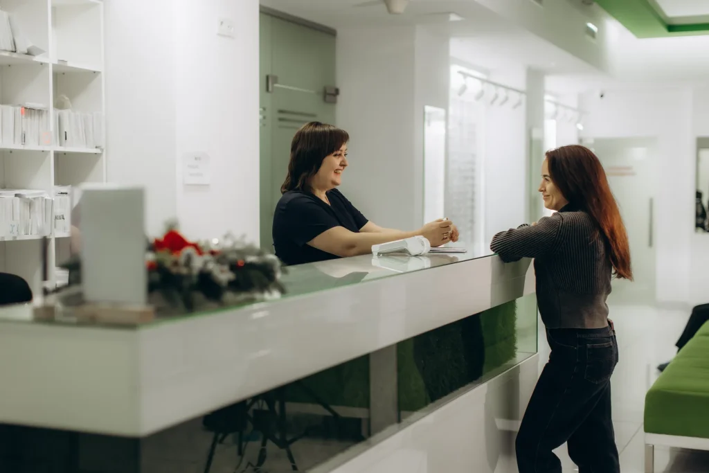 Clienta conversando con la recepcionista en el mostrador de una clínica