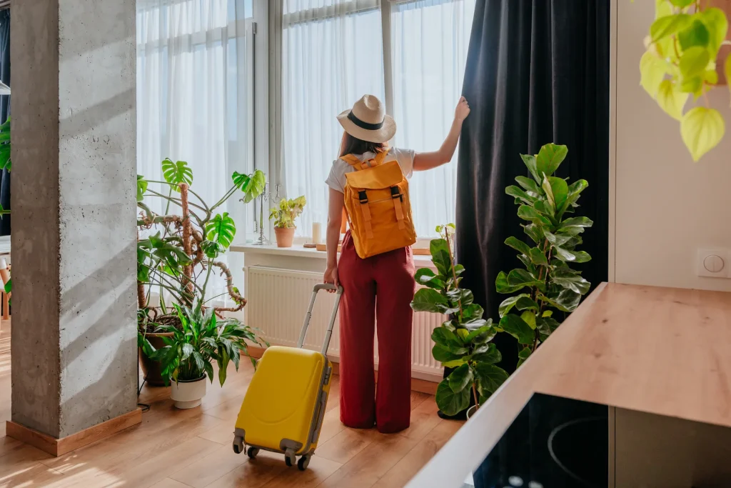 Viajera con maleta abriendo la cortina de un apartamento luminoso