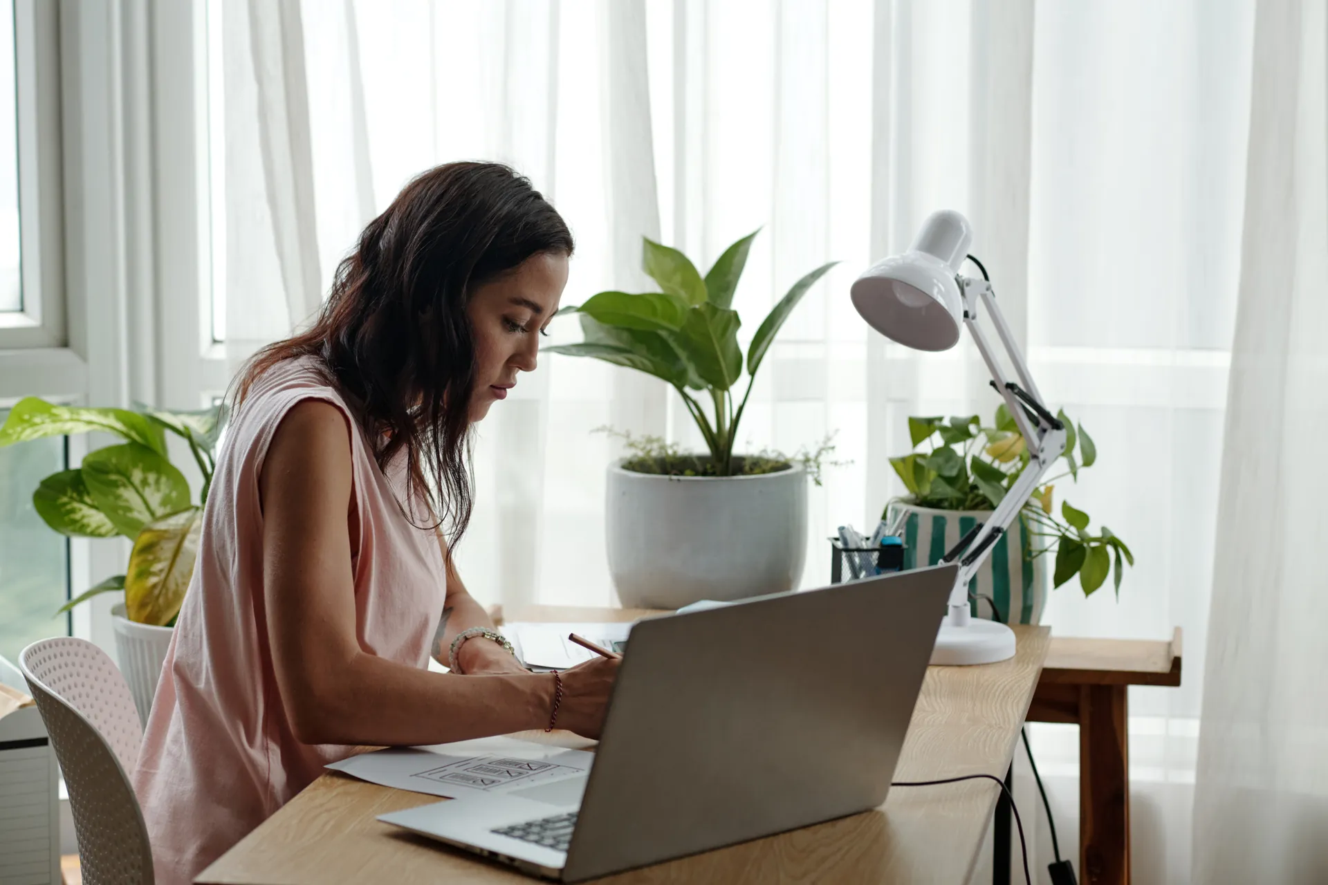Profesional tomando notas junto a su portátil en una mesa luminosa con plantas