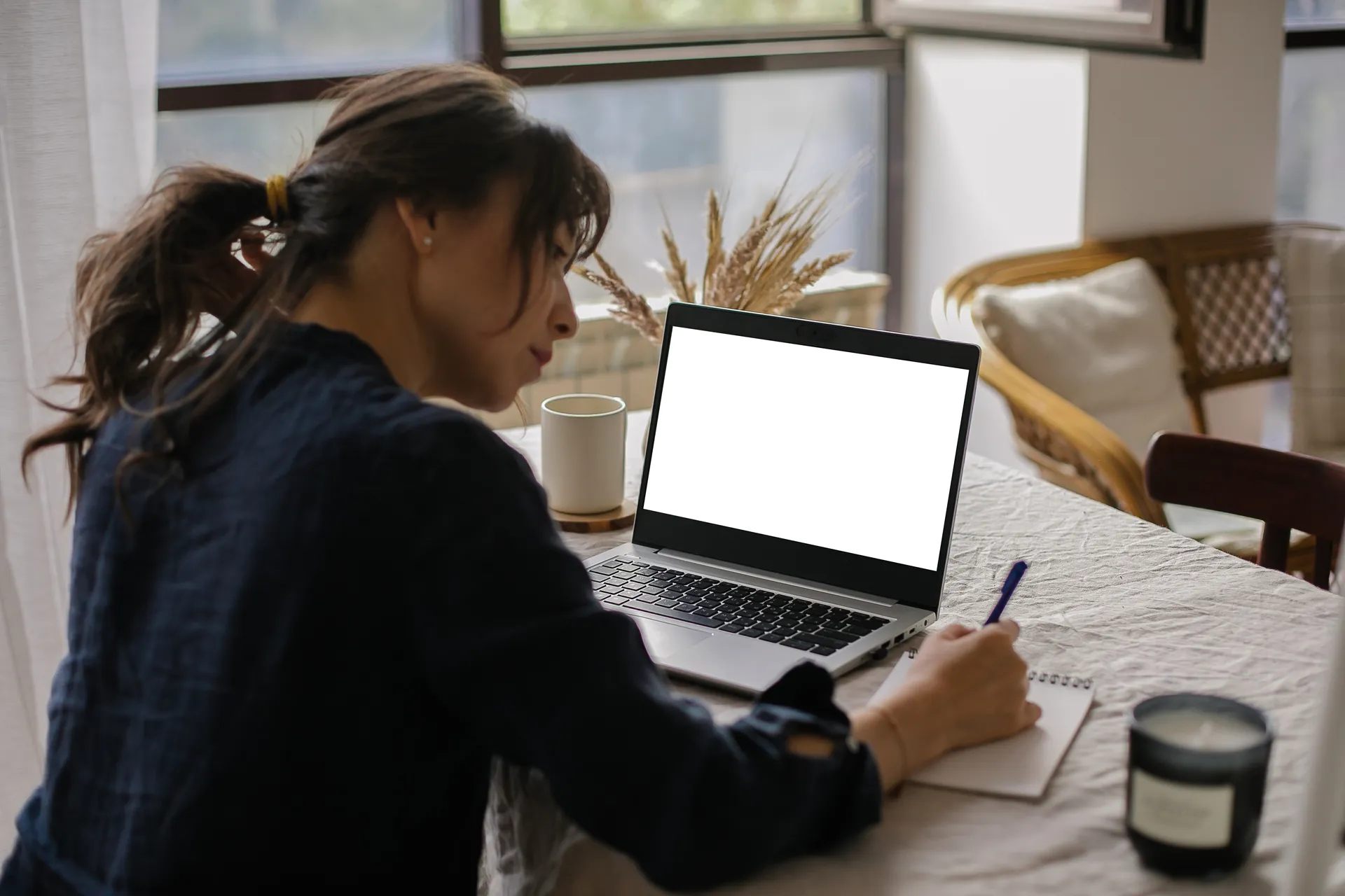 Mujer escribiendo en una libreta junto a su portátil en una mesa de casa