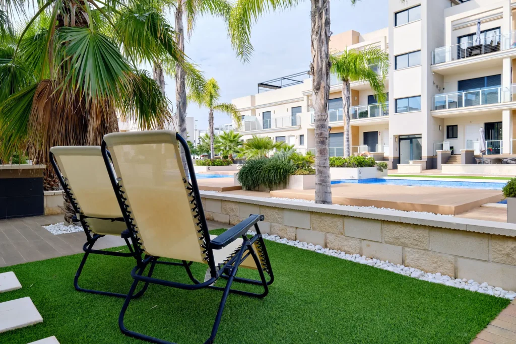 Tumbonas sobre el césped junto a la piscina comunitaria de una urbanización