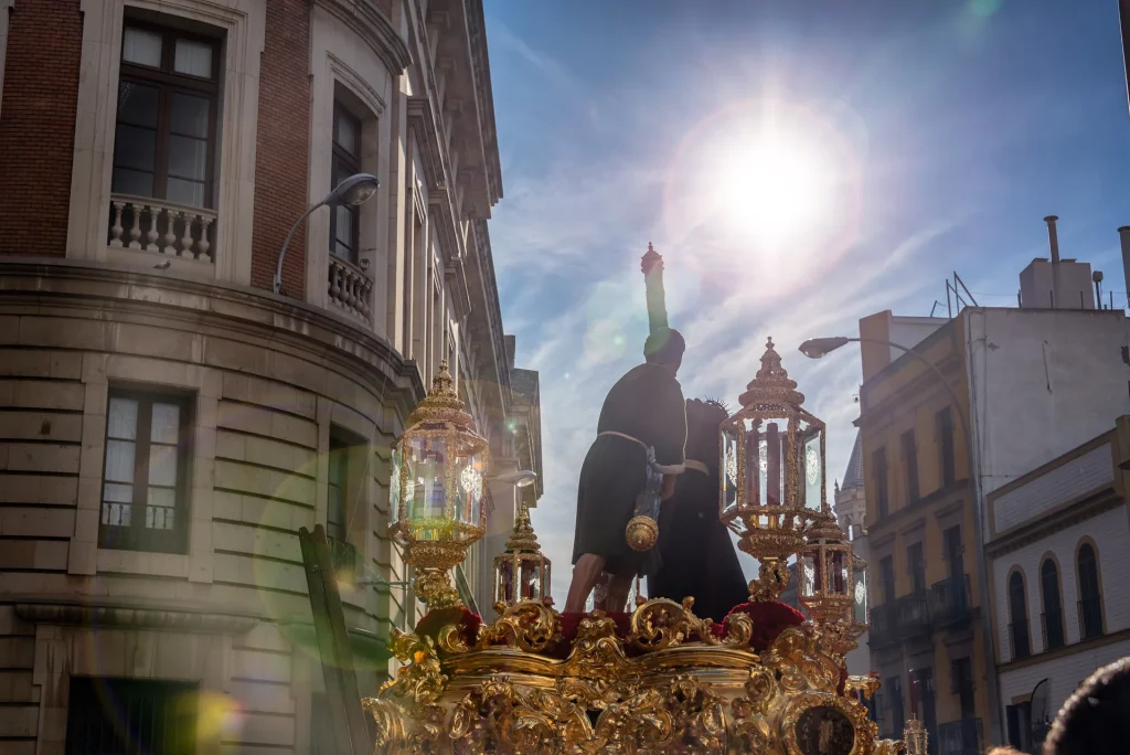 Paso de misterio dorado de una hermandad entre los edificios del centro en Semana Santa