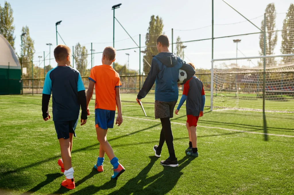 Entrenador caminando de espaldas con los niños de un club de fútbol base por el campo