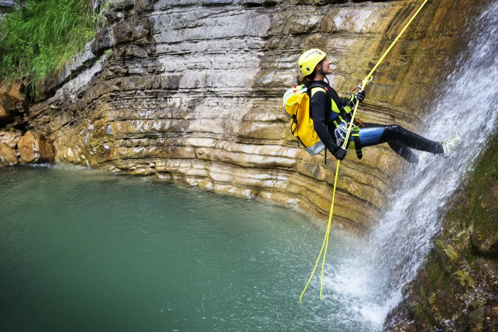Barranquista con casco descendiendo en rápel junto a una cascada