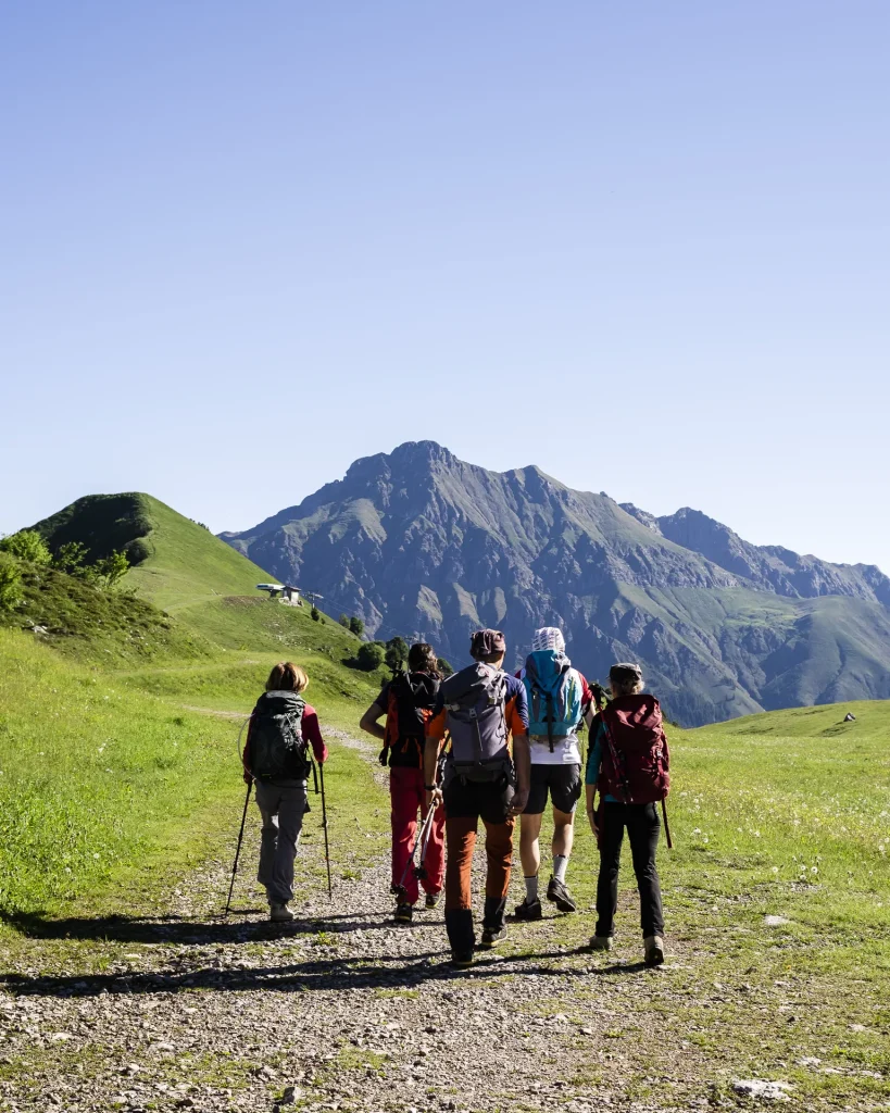Grupo de senderistas con mochilas y bastones caminando hacia un pico de montaña